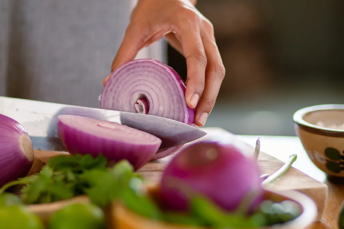 Hand slicing a fresh red onion for taco toppings.